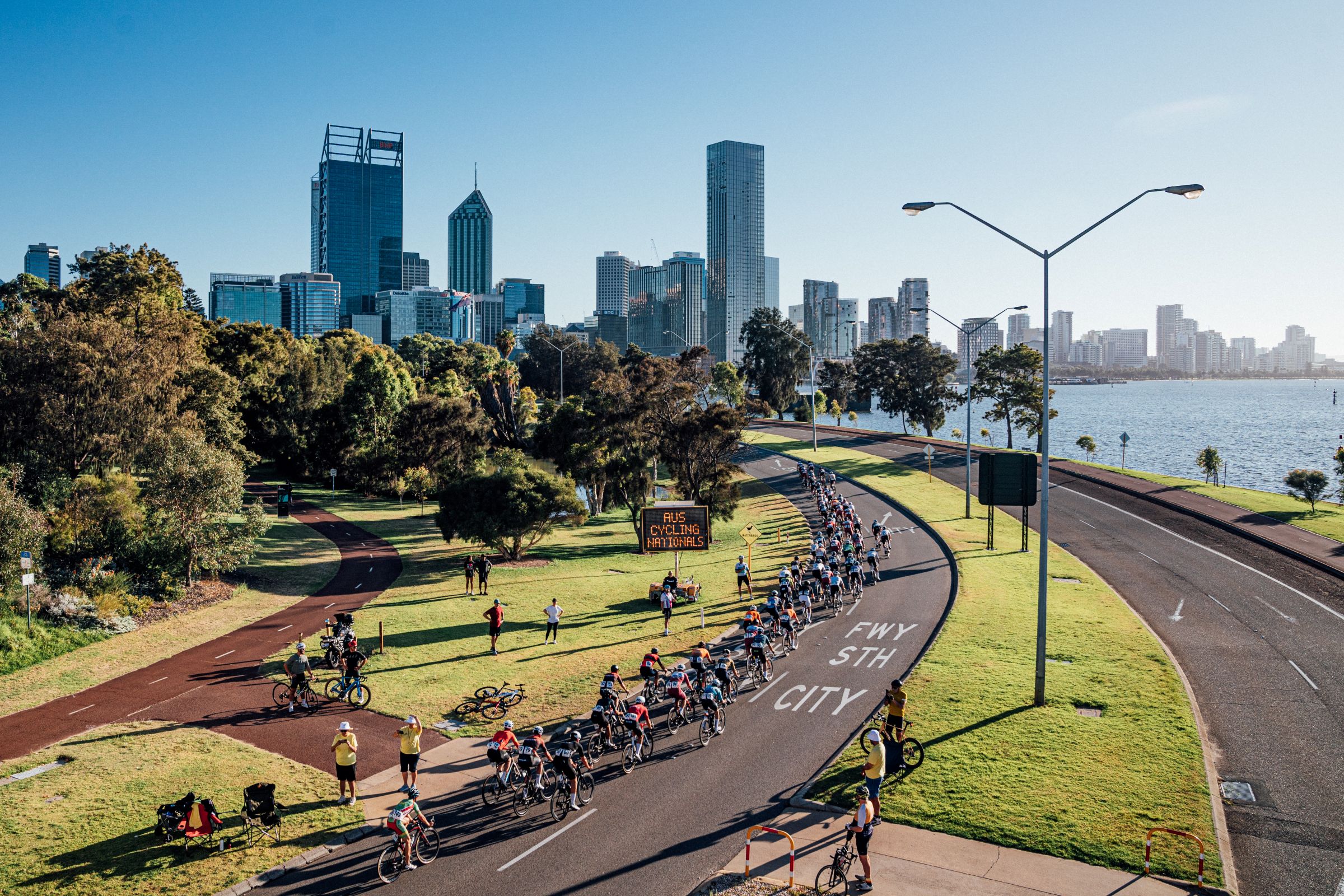 Cyclists on closed roads of Perth during the 2025 AusCycling Road National Championships riding towards the Perth CBD with the skyline in the background